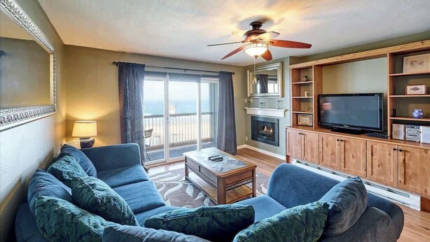 Ein Wohnzimmer mit Sofa, Fernseher, Kamin und einem Balkon mit Vorhängen.
