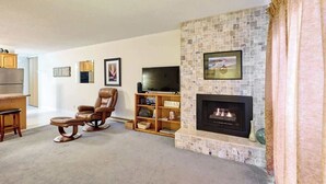 A living room with a fireplace, a television, a recliner, and a bookshelf.