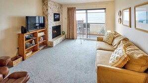 A living room with a TV, fireplace, sofa, and balcony with a view.