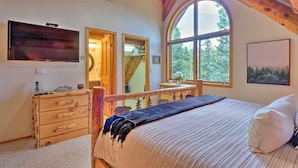 A bedroom with a large bed, wooden dresser, and a TV mounted on the wall.