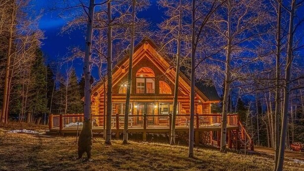 A log cabin with a deck, surrounded by trees.