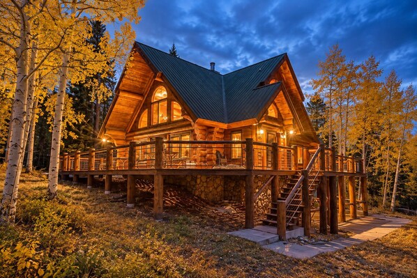 A log cabin with a wooden deck and a stone foundation, surrounded by trees.