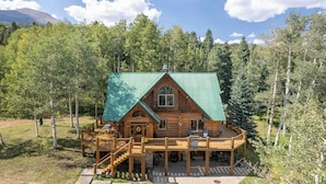 A log cabin with a green roof, wooden deck, and a stone foundation.