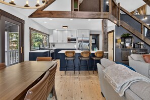 Une cuisine moderne avec des meubles blancs, un îlot central doté de tabourets de bar et un coin repas avec une table et des chaises en bois.