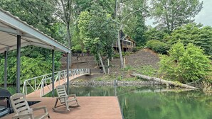 Une terrasse en bois avec des fauteuils à bascule, un espace abrité et un étang.