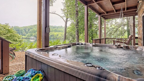 Un bain à remous avec une terrasse en bois et une vue sur un lac entouré d’arbres.