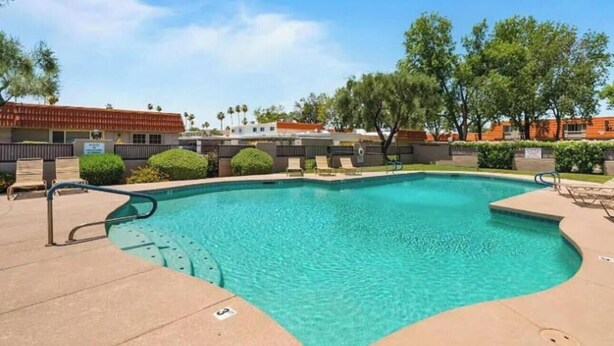 A swimming pool with lounge chairs, a clear blue sky, and buildings in the background. - Chaparral Charmer | 3BR | Pool | Bikes | King bed! (Scottsdale)