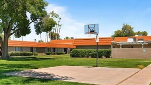 A basketball court with a hoop, surrounded by a grassy area and buildings with orange roofs. - Chaparral Charmer | 3BR | Pool | Bikes | King bed! (Scottsdale)