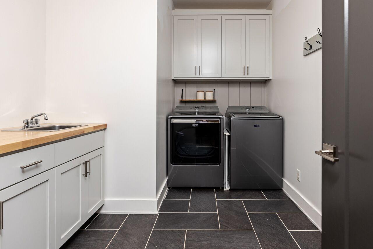 Een kleine keuken met witte kastjes, een roestvrijstalen spoelbak, een inbouwoven en een compacte koelkast.