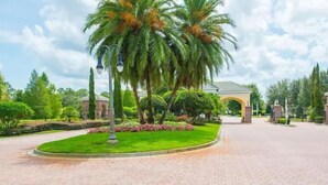 A landscaped entrance with palm trees, a paved pathway, and a building with a tiled roof in the background. - Modern Pool Villa on Guard Gated Golf Community with Conservation Views (Davenport)