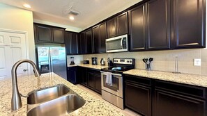 A kitchen with dark cabinets, stainless steel appliances, a granite countertop, and a double sink. - Modern Pool Villa on Guard Gated Golf Community with Conservation Views (Davenport)