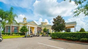 A large, yellow building with a central entrance, surrounded by palm trees and a well-maintained lawn. - Modern Pool Villa on Guard Gated Golf Community with Conservation Views (Davenport)