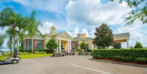 A large, yellow building with a central entrance, surrounded by palm trees and a well-maintained lawn. - Modern Pool Villa on Guard Gated Golf Community with Conservation Views (Davenport)