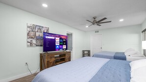 Una camera da letto con due letti, una TV montata su un supporto in legno e una ventola a soffitto.