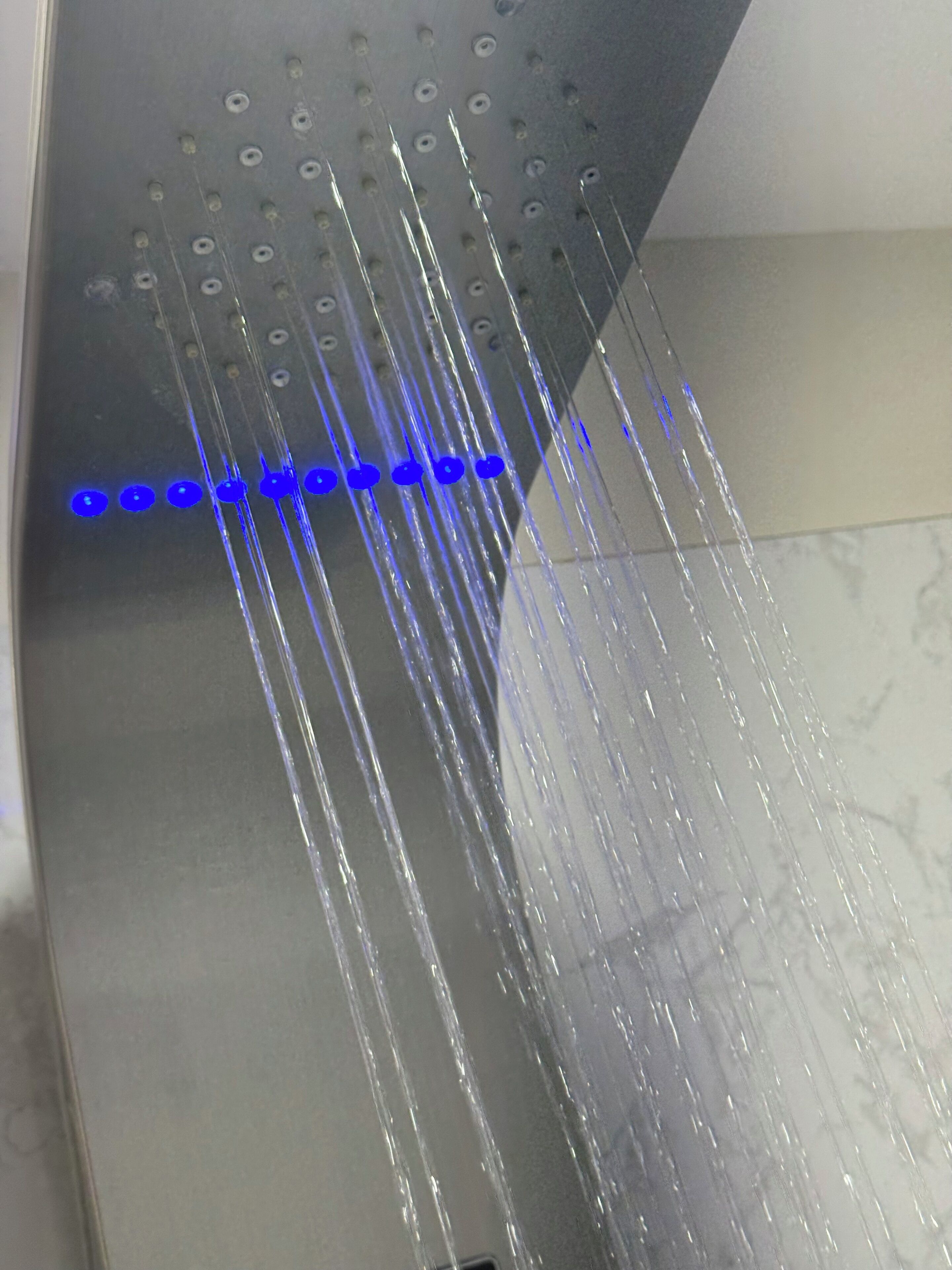 Une douche dotée de plusieurs jets d’eau et d’une bande lumineuse bleue.