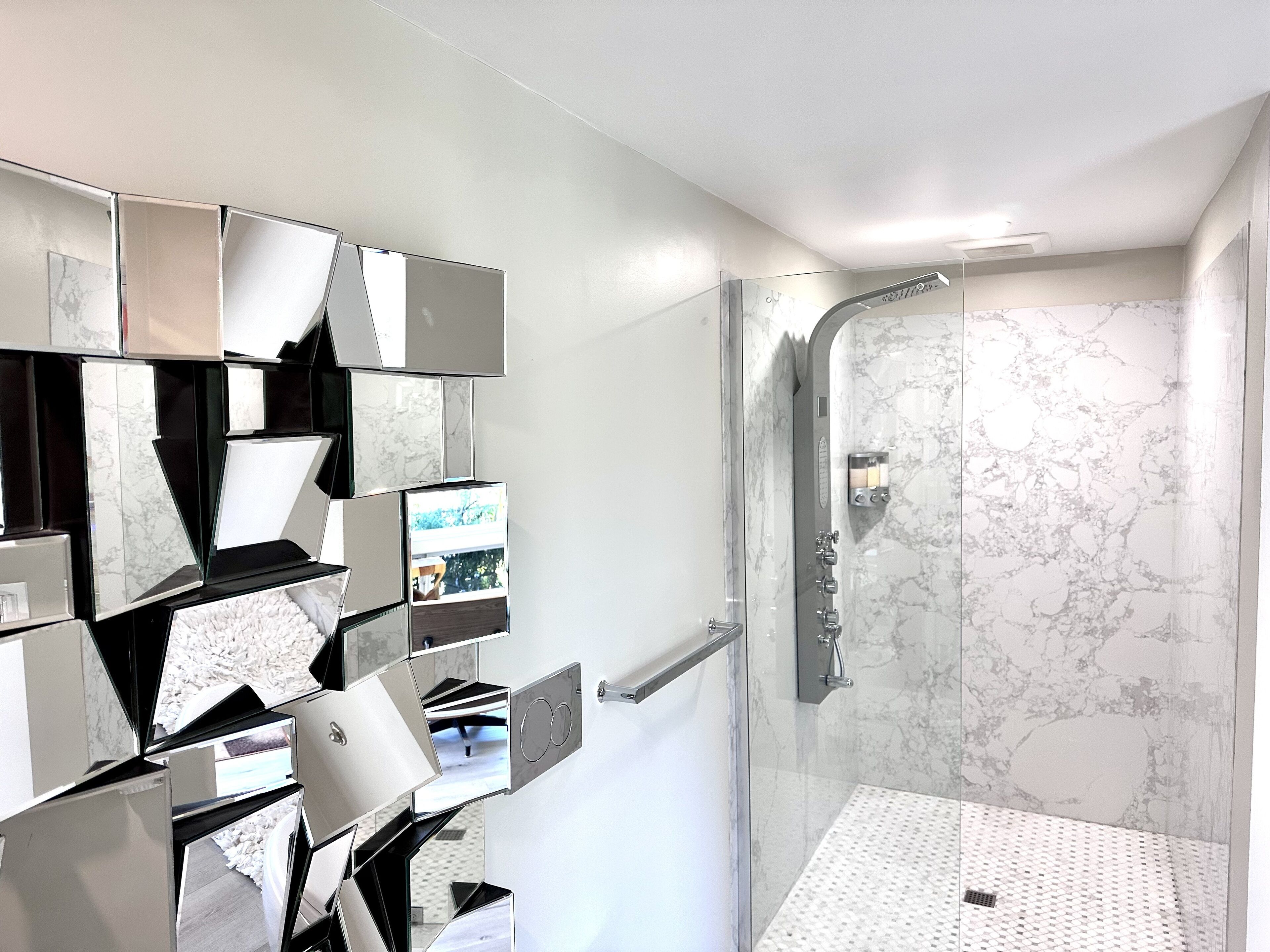 Un baño moderno con cabina de ducha de vidrio, salpicadero de mármol y espejo con motivos geométricos instalado en la pared.