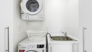 A laundry area with a front-loading washing machine, a drying machine, and a sink. - Kirra Beach 506 Pure Ocean Views (Coolangatta)