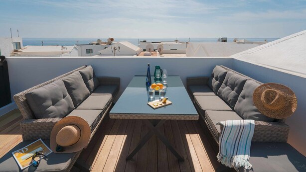 A rooftop terrace with a glass table, two cushioned sofas, and a view of the sea. - Lanzahost Villa Mimosa (Punta Mujeres)