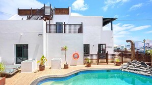 A white building with a swimming pool, a wooden deck, and a fenced area with potted plants. - Lanzahost Villa Mimosa (Punta Mujeres)