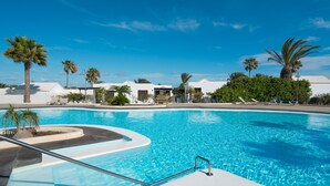 Una piscina con acqua cristallina azzurra, circondata da palme e un edificio bianco.