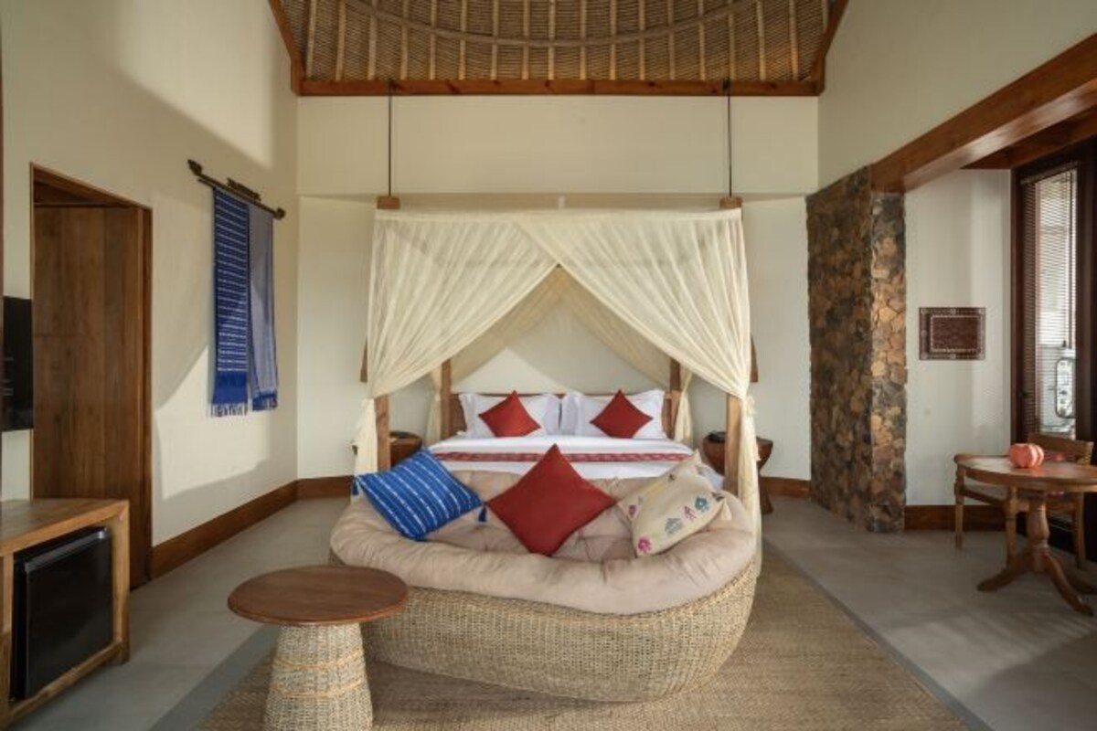 Una habitación con una cama bajo un dosel, una zona de estar circular, una mesita y un pilar de piedra.