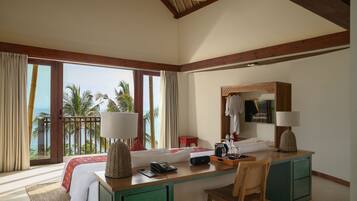 A hotel room with a large bed, a desk with a chair, a mirror, and a view of palm trees and the ocean.