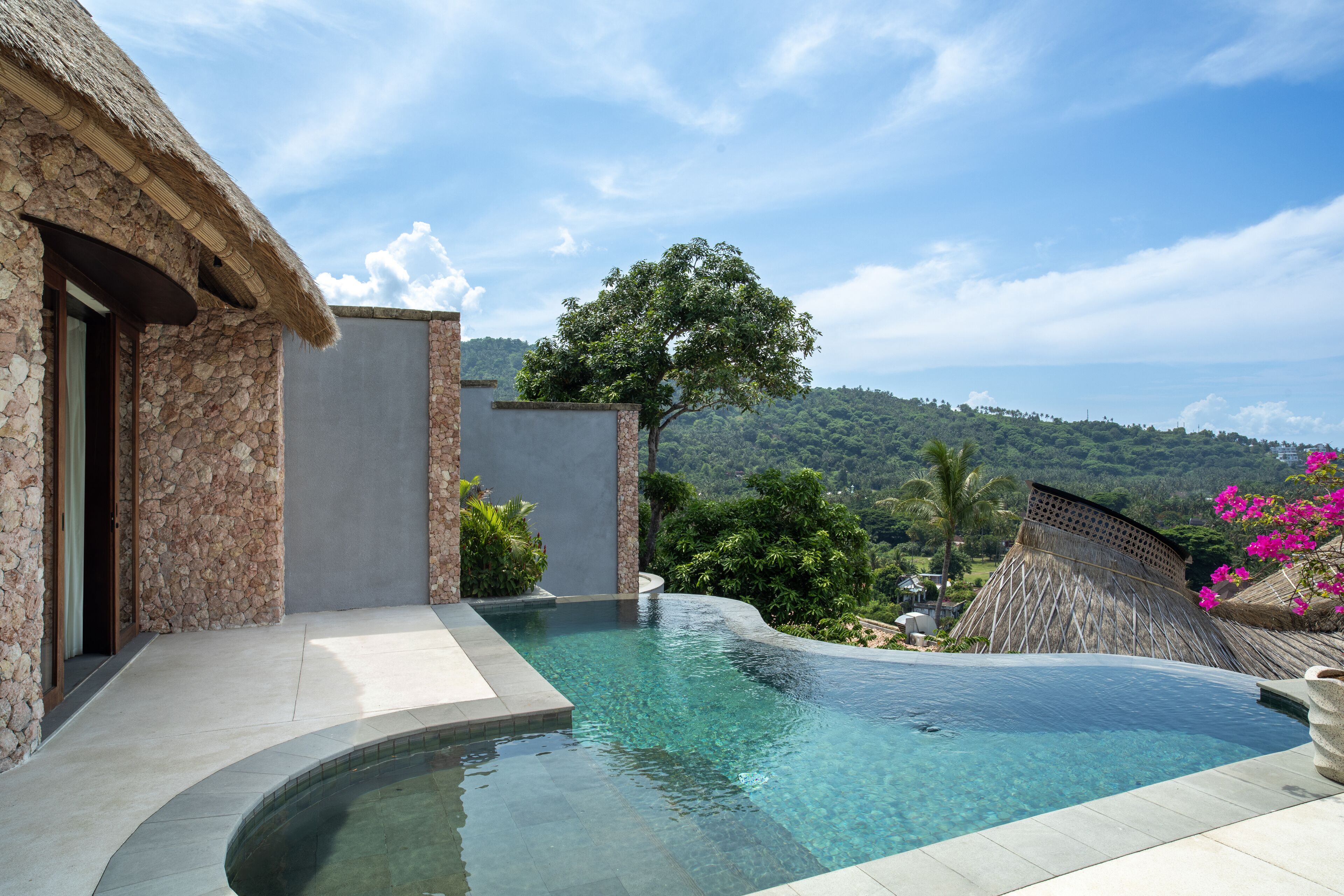Ein Infinity-Pool mit einer Steins- und Betonstruktur, umgeben von üppiger Vegetation und blauem Himmel.