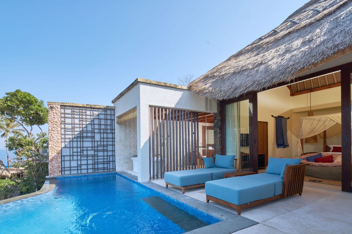 A poolside area with a thatched-roof structure, a lounge with blue cushions, and a stone wall.