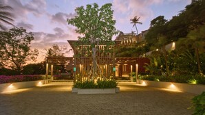 Un edificio moderno con un árbol central, rodeado de senderos bien iluminados y abundante vegetación.