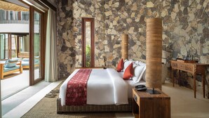 Un dormitorio amplio con una cama grande, una pared de piedra, una mesita de noche de madera y vistas a una zona de estar exterior a través de una puerta de cristal.