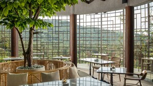 Un restaurante con amplios ventanales, mobiliario de mimbre y un árbol central.