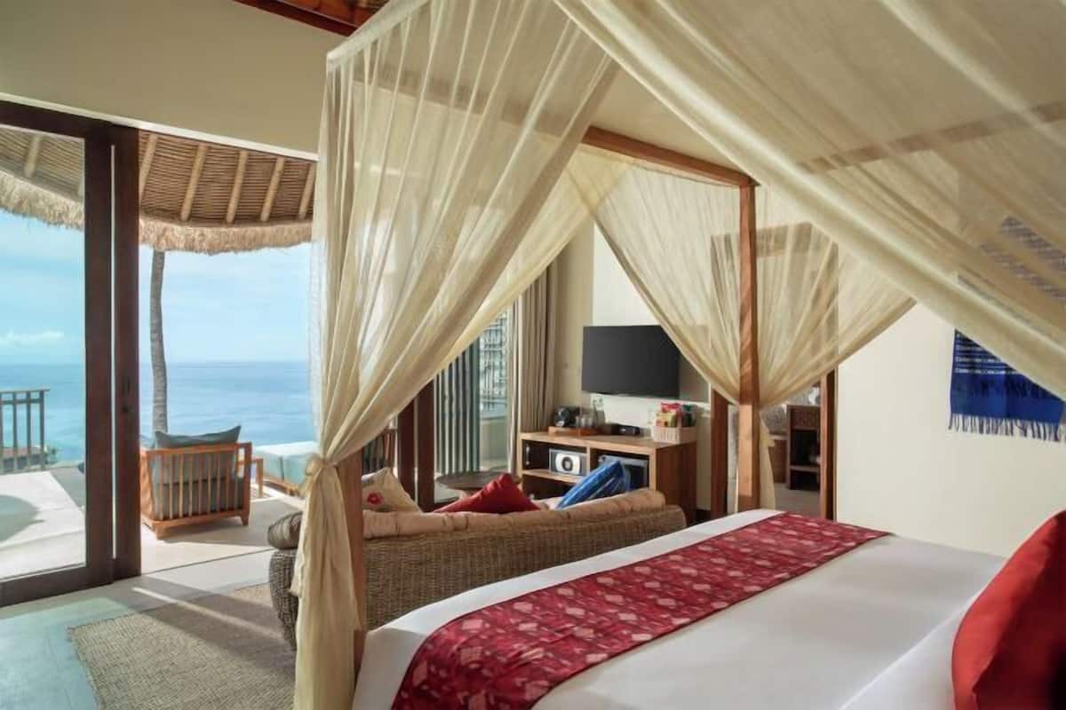 A bedroom with a bed, a TV, and a view of the ocean.