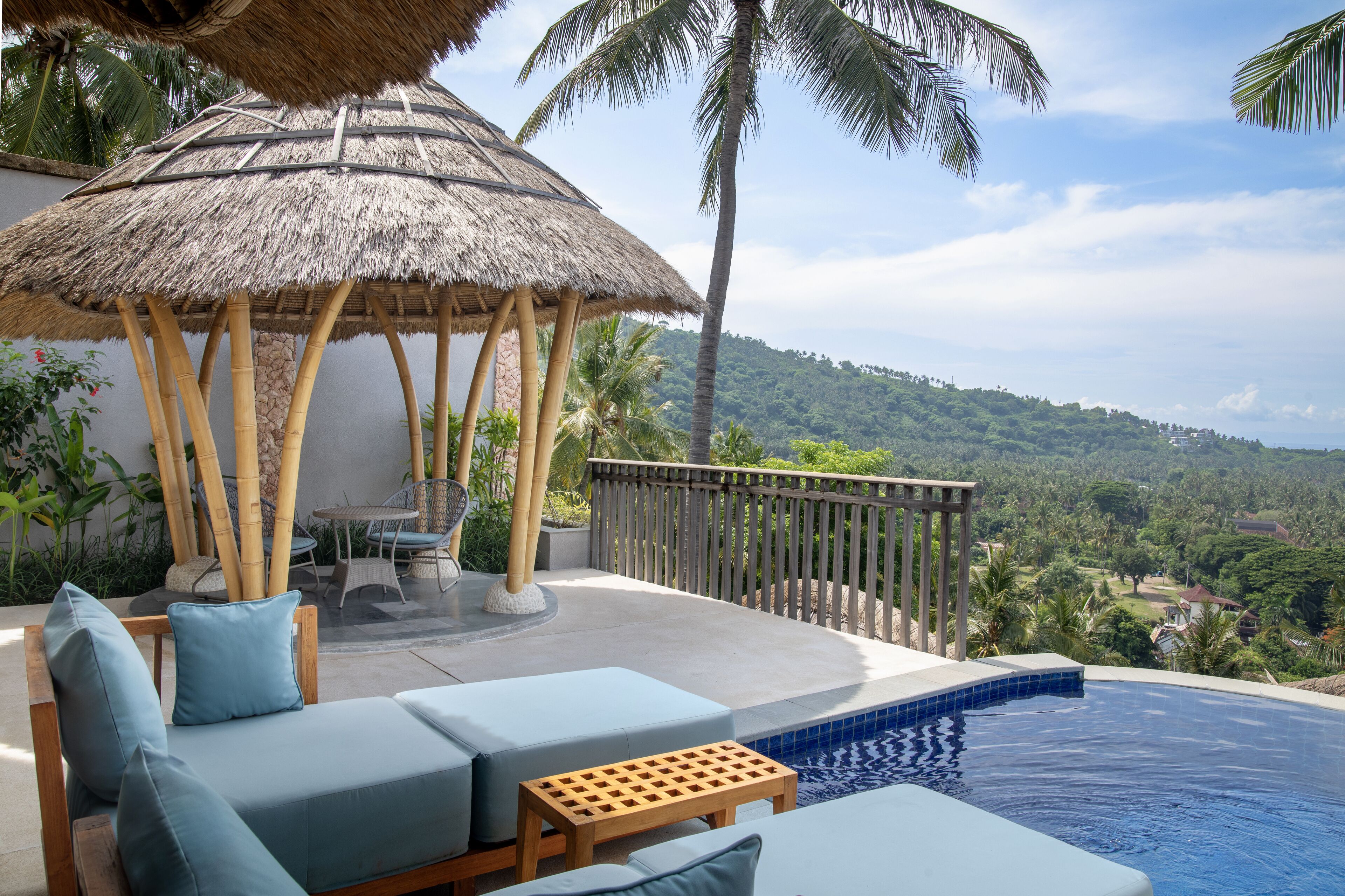 A poolside area with a thatched umbrella, lounge chairs, and a view of a lush landscape.