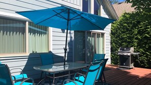 En terrasse med et glasbord, blå stole, en blå parasol og en grill.