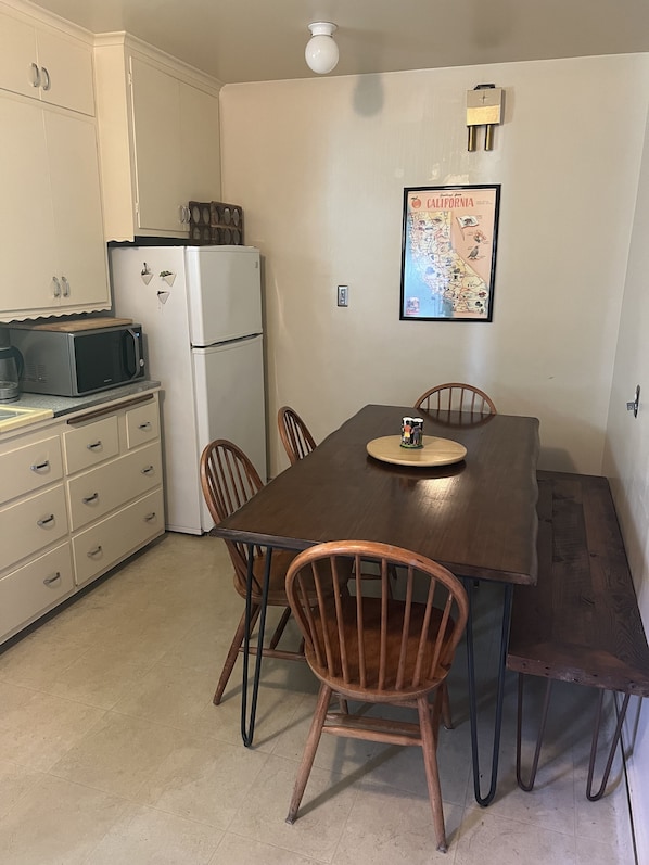 A compact kitchen with a dining table, chairs, a refrigerator, a microwave, and cabinets.