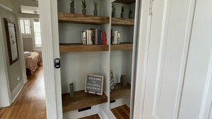Een hal met houten vloeren, witte muren en ingebouwde planken met boeken en kleine planten.