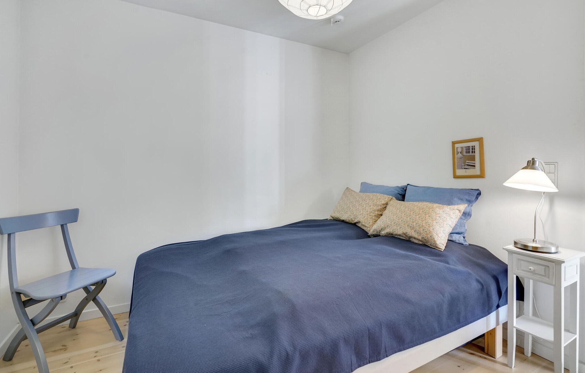 Una camera da letto con un letto, una sedia, un comodino con una lampada e un quadro appeso al muro.