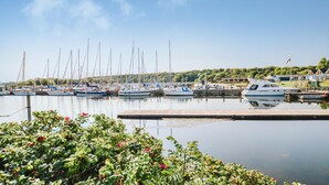 A marina with multiple sailboats docked, a wooden pier, and a backdrop of greenery and buildings.
