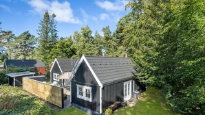A two-story wooden house with a dark roof, surrounded by lush greenery and trees.