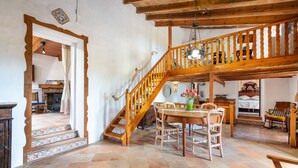 A spacious room with a wooden staircase, a dining area with a table and chairs, and a view of the kitchen in the background.