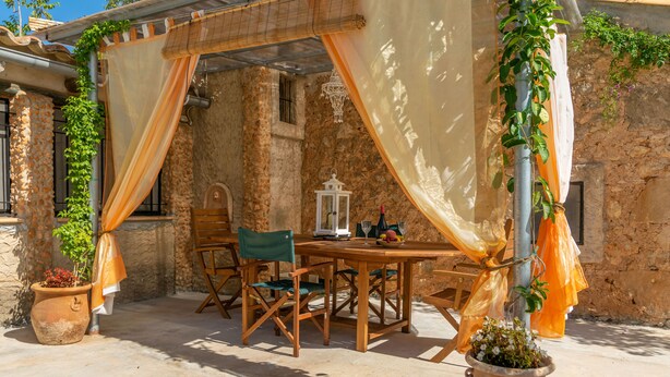 An outdoor patio with a wooden table and chairs, a lantern, and potted plants.