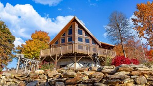 Eine Holzhütte mit Balkon, umgeben von Herbstlaub und einer Steinmauer.