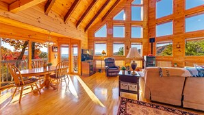 Eine geräumige Holzhütte mit Essbereich, einem Wohnzimmer mit Sofa und großen Fenstern mit Blick ins Freie.