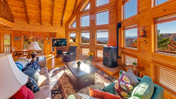 Ein geräumiges Holzblockhaus-Interieur mit mehreren Fenstern, einem Kamin und einer gemütlichen Sitzecke.