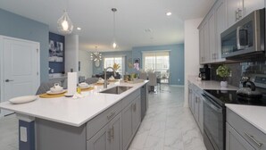 A modern kitchen with a large island, stainless steel appliances, and pendant lighting.