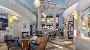 A spacious lobby with high ceilings, wooden beams, and a central seating area with wicker chairs and a coffee table.