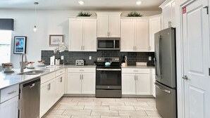 A modern kitchen with white cabinets, a stainless steel dishwasher, a black oven, a microwave, and a refrigerator.