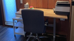 A small office space with a wooden desk, a chair, a printer, and a wall-mounted light fixture. - One Bedroom Cottage (Half Moon Bay)