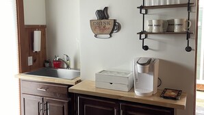 A kitchen with a wooden countertop, a coffee maker, a clock, and a shelf with glassware. - One Bedroom Cottage (Half Moon Bay)