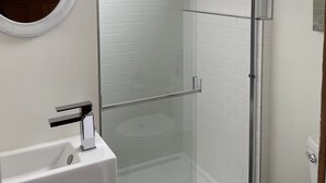 A bathroom with a glass shower enclosure, a white sink, and a mirror with an ornate frame. - One Bedroom Cottage (Half Moon Bay)